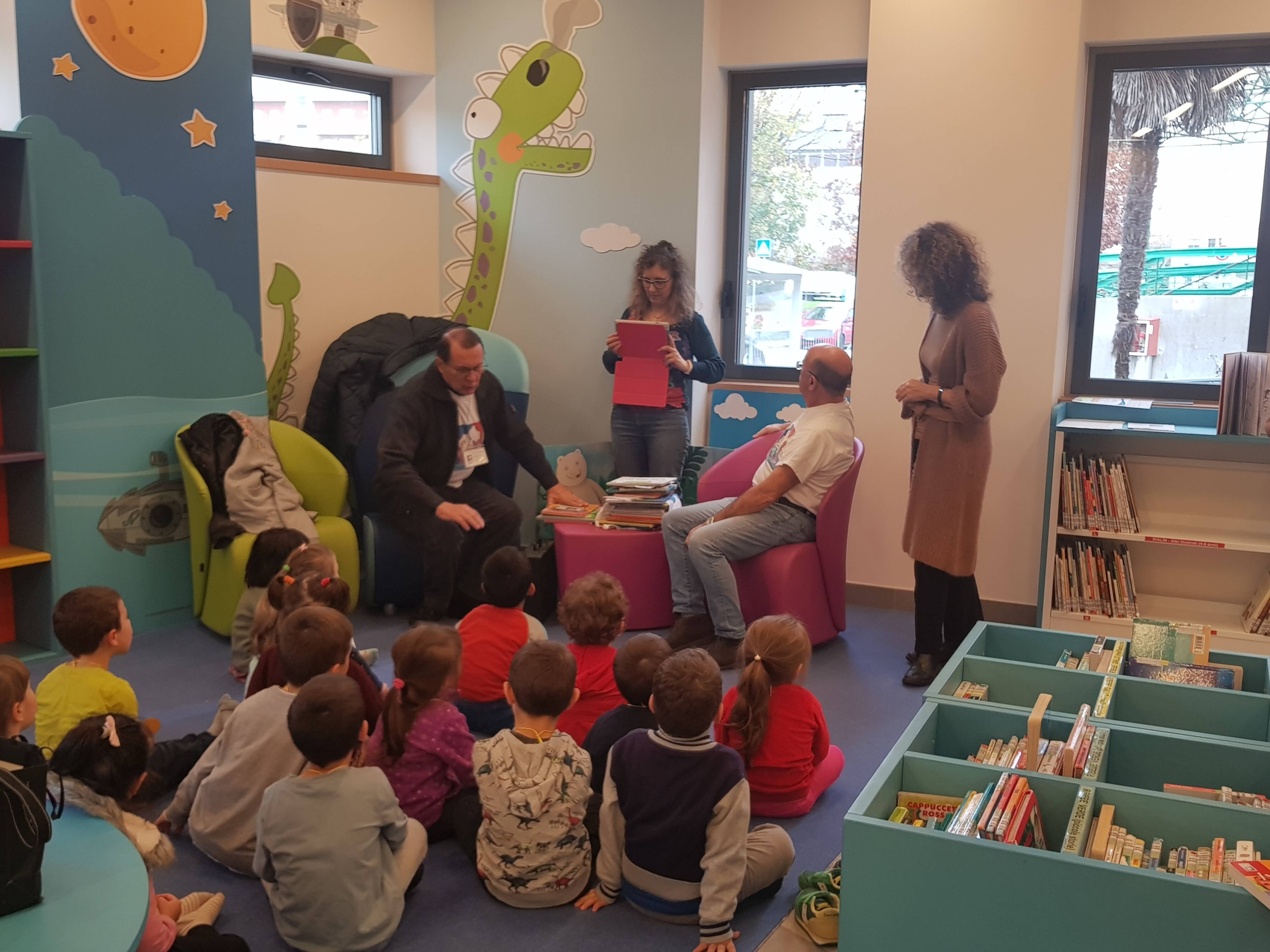 bambini seduti in biblioteca che ascoltano letture ad alta voce
