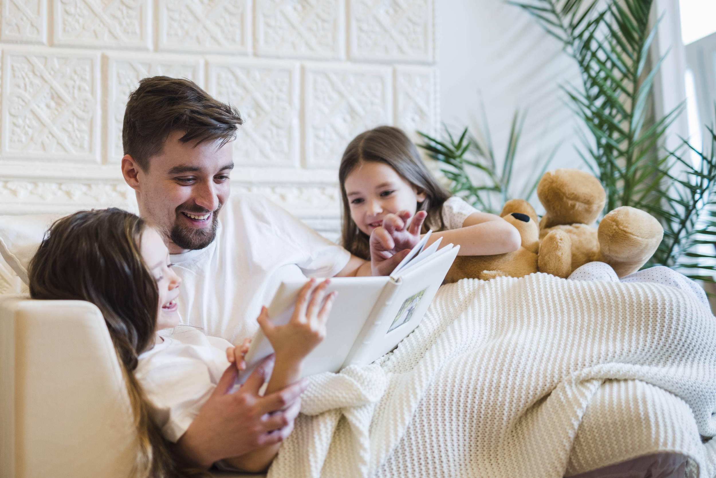 Immagine con padre che legge un libro alle due figlie