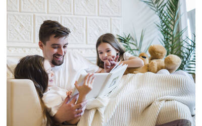 Immagine con padre che legge un libro alle due figlie